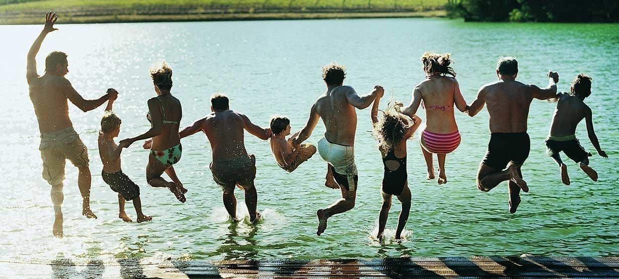 Rückansicht einer großen Familiengruppe, die gemeinsam in einen See springt