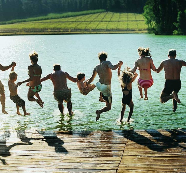 Rückansicht einer großen Familiengruppe, die gemeinsam in einen See springt