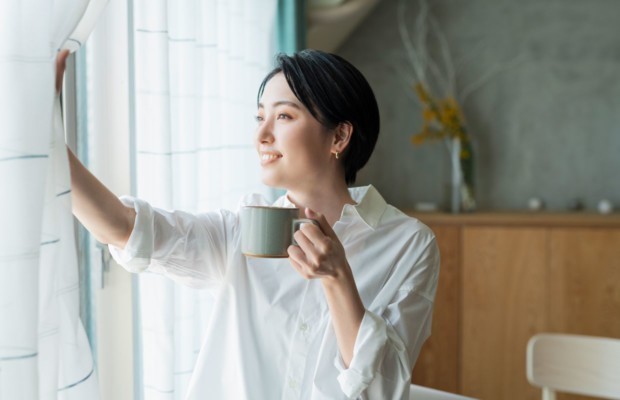 Eine Frau, die aus dem Fenster schaut und Kaffee trinkt