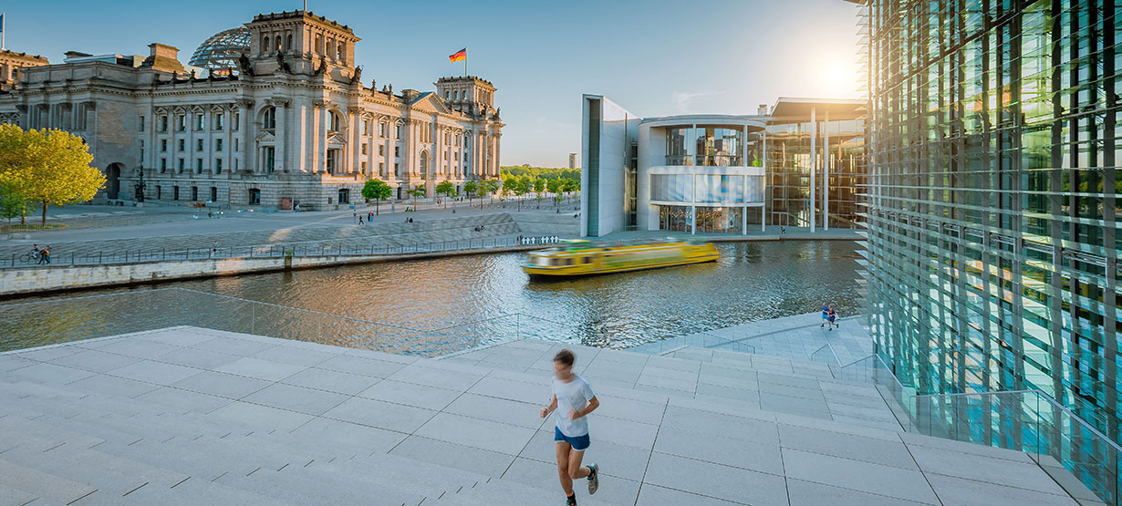 Ein Mann läuft an der Spree, im Hintergrund sieht man den Reichstag