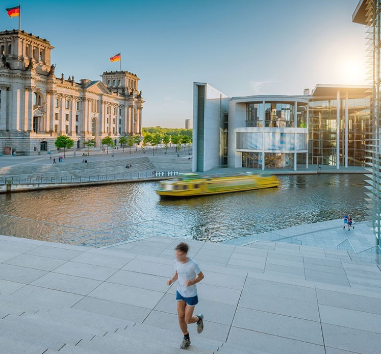 Ein Mann läuft an der Spree, im Hintergrund sieht man den Reichstag