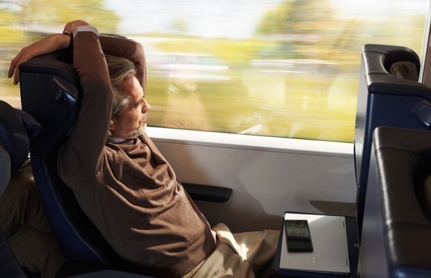 Mann im Zug schaut aus dem Fenster, Smartphone Handy liegt auf einem Tisch